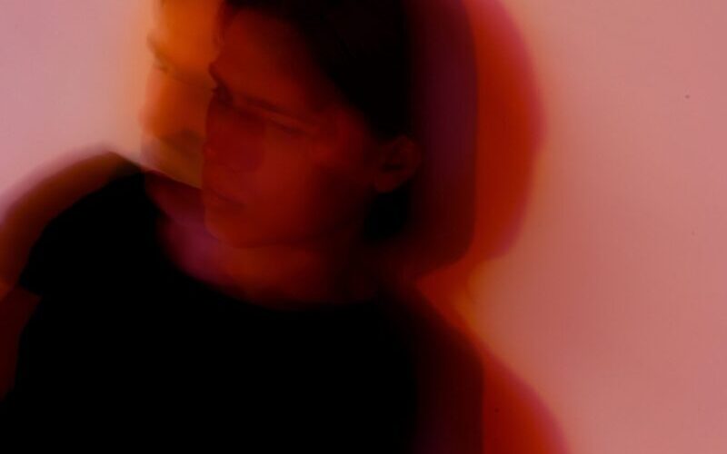 Defocused anonymous young anxious male with split personality standing near wall with shade in twilight while looking away